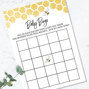 May include: A printable baby shower bingo card with a honeycomb pattern and bee illustrations. The text reads "Baby Bingo" and "Fill in each square with a gift you think the mother-to-be will receive. Five in a row wins!"