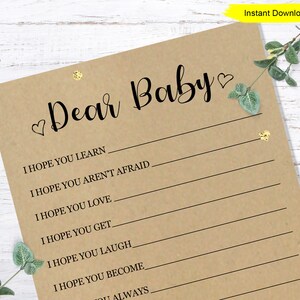 May include: A printable baby shower game card with the text "Dear Baby" and a list of things the guest hopes the baby will learn, love, and become. The card has a brown background with gold glitter hearts.