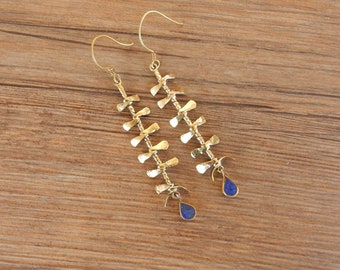 May include: Gold earrings with a delicate, layered design featuring small, twisted metal pieces. Each earring is adorned with a blue gemstone drop.