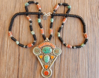 May include: A handcrafted necklace featuring a silver pendant with turquoise and coral accents. The necklace has a black beaded chain with turquoise and coral beads. The text "kc594" is in the upper left corner.