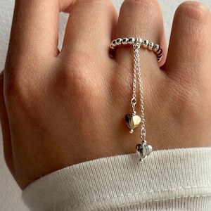 Puede incluir: Un anillo de plata con una banda de cuentas y dos colgantes de corazón. Un colgante es de plata y el otro de oro.