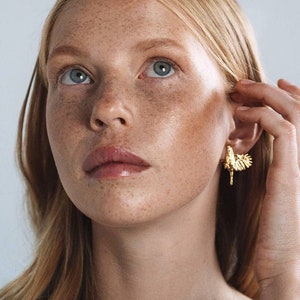 May include: A close-up of a woman's face with freckles. She is wearing a gold earring with a bird design.