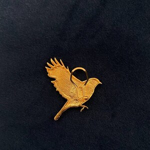 May include: Gold-coloured metal bird brooch with a detailed design. The brooch has a hinged clasp on the back.