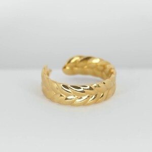 May include: A gold-toned ear cuff with a leaf-like design. The cuff is made of metal and has a smooth, polished finish.