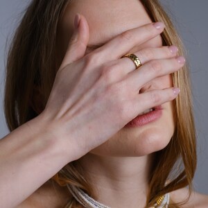 May include: A woman wearing a gold ring and a multi-strand pearl necklace with gold accents.