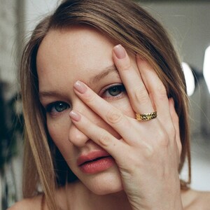 May include: A close-up of a person's hand wearing a gold ring with a braided design. The ring is on the index finger and the person's hand is covering their eye.