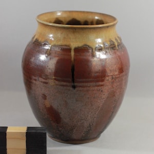 May include: A brown ceramic vase with a yellow glaze and a drip glaze effect. The vase has a rounded body and a wide mouth.