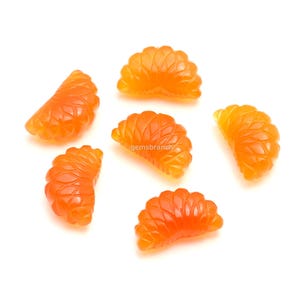Puede incluir: Rodajas de gemas de color naranja, que se asemejan a gajos de mandarina, se disponen sobre un fondo blanco. Las gemas talladas tienen una superficie texturizada, con detalles visibles. La imagen está bien iluminada, resaltando la calidad translúcida de las piedras.