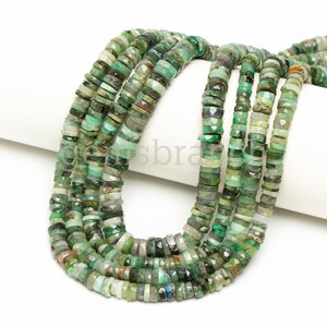 May include: A strand of green gemstone beads, with a faceted, irregular shape. The beads are strung on a white cord and are arranged in a loose, flowing pattern.