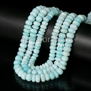 Peut inclure: Un brin de perles de pierres précieuses bleu clair. Les perles sont rondes et ont une forme légèrement irrégulière. Elles sont enfilées sur un fil transparent.