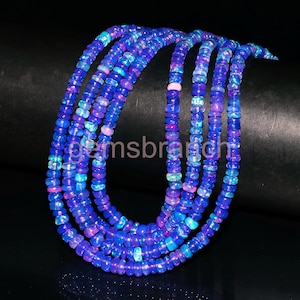 May include: A strand of blue and purple opal beads. The beads are round and have a iridescent sheen. The beads are strung on a clear thread.