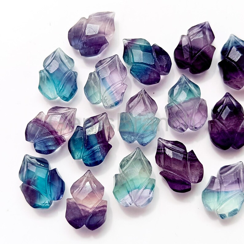 Puede incluir: Una colecci&oacute;n de gemas facetadas en forma de flor, en tonos morados, azules y verdes. Las gemas est&aacute;n dispuestas sobre una superficie blanca, mostrando sus intrincados cortes y variaciones de color. Estas piedras decorativas son ideales para la creaci&oacute;n de joyas.