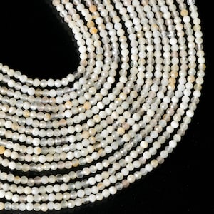 以下が含まれることがあります： 白いムーンストーンビーズのストランド。各ビーズはファセットカットされており、わずかに虹色の輝きを放っています。
