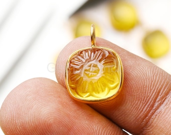 Puede incluir: Un colgante dorado con forma cuadrada y un diseño floral tallado. El colgante tiene un lazo en la parte superior para una cadena. La piedra preciosa es de color amarillo translúcido.