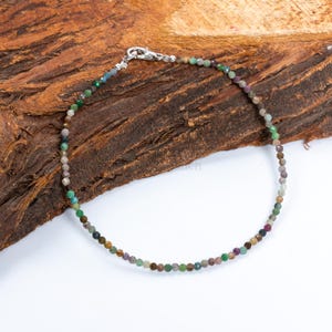 Peut inclure: Un bracelet de perles délicat avec de petites pierres précieuses multicolores. Le bracelet est monté sur un cordon fin et souple et sécurisé par un fermoir argenté. Les pierres précieuses sont de différentes nuances de vert, de marron et de violet.