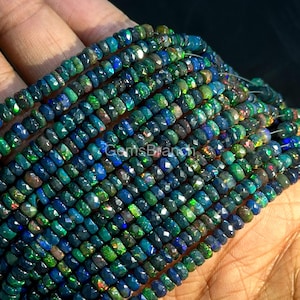 May include: Strands of faceted, dark opal beads in shades of blue, green, and black. The beads are strung together, creating a textured and colorful display. The image shows a close-up view of the beads, highlighting their iridescent qualities.