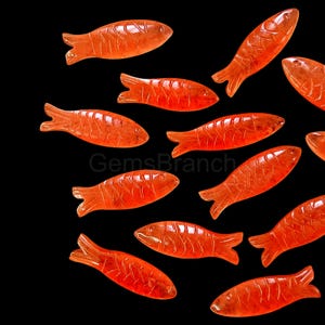 Puede incluir: Una colección de 12 amuletos de peces naranja tallados. Los peces están hechos de un material translúcido y tienen un diseño detallado.