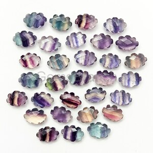 May include: A collection of 25 oval-shaped fluorite gemstones with a scalloped edge. The stones are a mix of purple, green, and white.