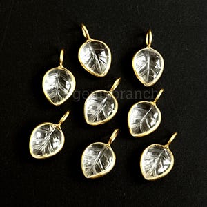 May include: A collection of leaf-shaped pendants. Each pendant features a clear, leaf-veined design encased in a gold-colored metal frame. The pendants are displayed against a black background, highlighting their intricate details.