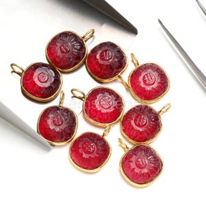 May include: A collection of red gemstone pendants with a floral design and gold-colored metal settings. Each pendant has a loop for attaching to a chain or other jewelry component. The gemstones are a deep red color.