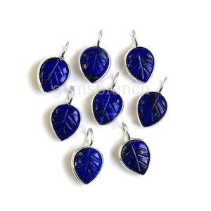 Könnte beinhalten: Neun silberne, blattartige Anhänger mit blauen Lapislazuli-Edelsteinen. Jeder Anhänger hat ein geschnitztes Blattdesign.