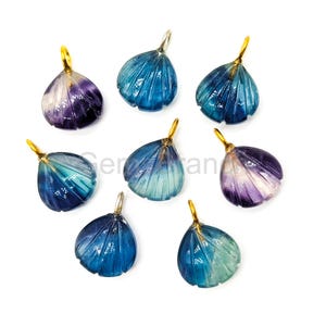 以下が含まれることがあります： 青、ターコイズ、紫の色合いの宝石ペンダントのコレクション。各ペンダントは、彫刻されたディテールと金色のベイルを備えた花びらのような形をしています。ペンダントは白い背景に配置されています。