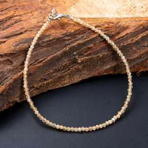 Peut inclure: Un bracelet délicat composé de petites perles rondes jaune clair enfilées ensemble. Le bracelet est doté d'un fermoir argenté. Le fond est une surface sombre avec un morceau de bois.