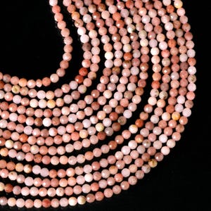 May include: A strand of pink and red gemstone beads. The beads are faceted and have a round shape. The beads are strung on a clear thread.