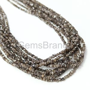 May include: A strand of brown rough diamond beads. The beads are small and irregular in shape, and they are strung together on a clear thread. The beads are arranged in a loose, flowing pattern.