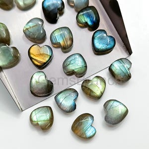 May include: A collection of heart-shaped labradorite gemstones in various shades of blue, green, and gold. The stones are arranged on a silver tray.