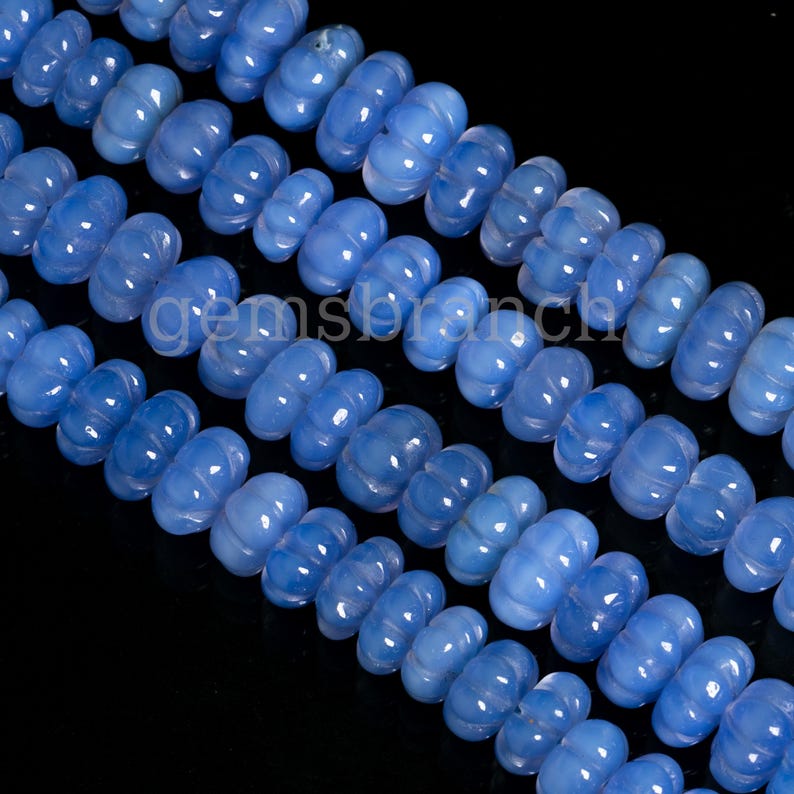 May include: A strand of light blue gemstone beads with a faceted, pumpkin-shaped design. The beads are strung together on a clear thread.