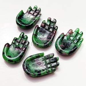 Może przedstawiać: Pięć rzeźbionych rzeźb dłoni z kamieni szlachetnych. Dłonie są zielone z ciemnoczerwonymi i czarnymi wtrąceniami. Każda dłoń jest wklęsła, ze szczegółowymi palcami i gładkim, wypolerowanym wykończeniem. Dłonie są ułożone na białej powierzchni.