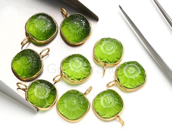 Puede incluir: Una colección de nueve colgantes de piedras preciosas verdes con un diseño floral y un borde de metal dorado. Cada colgante tiene un lazo para sujetarlo a una cadena u otro componente de joyería. Los colgantes se muestran sobre una superficie blanca.