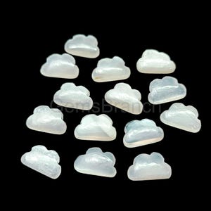 May include: A selection of cloud-shaped gemstones in shades of white and pale blue, set against a black backdrop. The gemstones have a smooth, polished finish, creating a delicate and ethereal aesthetic. The gemstones are likely for jewelry making.
