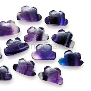 May include: A collection of cloud-shaped fluorite gemstones in shades of purple, blue, and white. The polished stones have a smooth, glossy finish and are arranged on a white surface. These decorative stones are ideal for jewelry making or collecting.