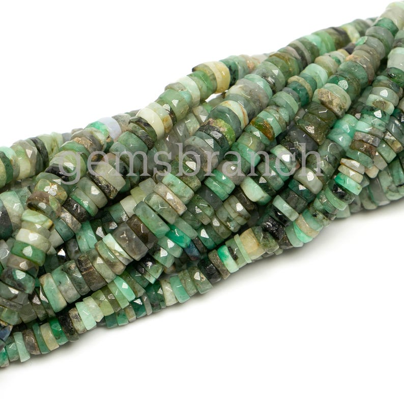 May include: A strand of green emerald gemstone beads. The beads are faceted and have a slightly irregular shape. They are strung on a clear thread.