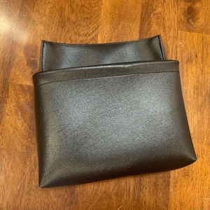 May include: A black leather pouch with a fold-over flap. The pouch is closed and sitting on a wooden surface.