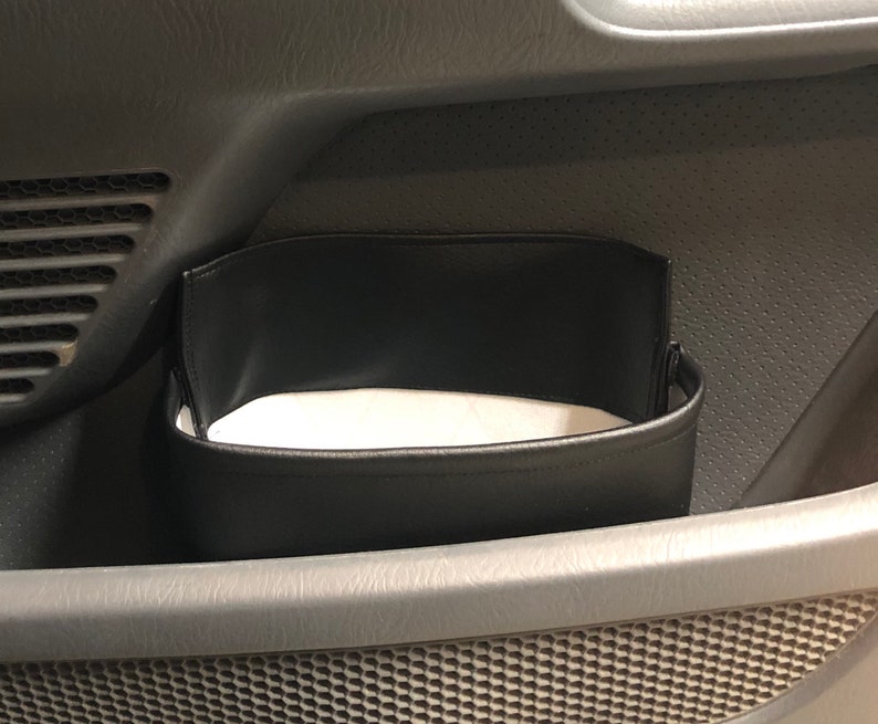 May include: Black leather car organizer hanging in a car door pocket. The organizer has a white fabric lining.