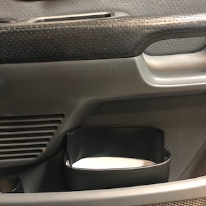 May include: A black leather organizer pouch hangs inside the door of a car. The pouch is empty and has a white fabric lining.