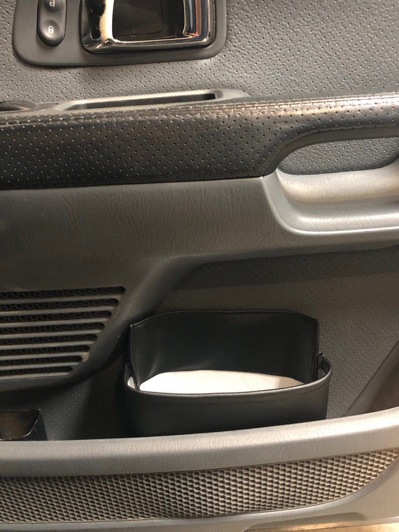 May include: A black leather organizer pouch hangs inside the door of a car. The pouch is empty and has a white fabric lining.