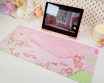 Puede incluir: Un ratón de ordenador rosa y verde con una escena de invierno. La escena incluye una casa de jengibre, un reno y un pequeño personaje con alas. El ratón de ordenador está sobre un escritorio blanco con una tableta y otras decoraciones.