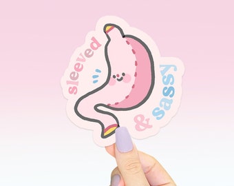 May include: Pink and blue sticker featuring a cartoon stomach with a stitched line and a happy face. The text on the sticker reads "sleeved & sassy".