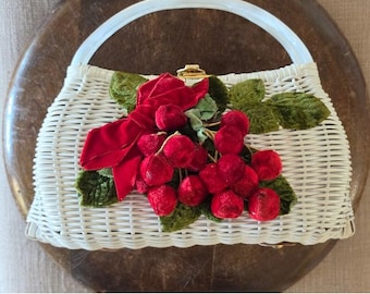 Peut inclure: Un sac à main en osier tressé blanc avec une poignée supérieure et un fermoir en métal doré. L'avant est orné d'une grappe de cerises en velours rouge, de feuilles en velours vert et d'un nœud en velours rouge fixé au centre du tressage.