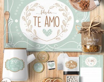 Könnte beinhalten: Ein blaugrünes und weißes Tischset mit einem Herz und dem Text "Feliz dia TE AMO". Ein weißer Krug mit einem braunen Griff und einem Etikett mit der Aufschrift "Love is all you need". Ein Glas mit einem braunen Etikett mit der Aufschrift "Aca hay amor!" und ein brauner und weißer Teebeutel mit einem Herz und dem Text "Love".