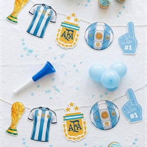 May include: A party banner featuring two repeating sets of cutouts: a gold trophy, a blue and white striped jersey, an AFA crest with three stars, a soccer ball with the Argentina flag design, and a blue foam finger with the text #1.