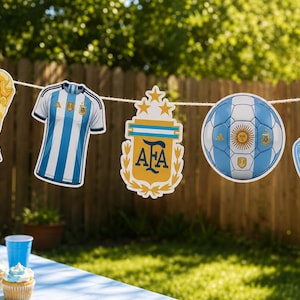 May include: A decorative party banner featuring five cutouts hanging on a string: a gold trophy, a blue and white striped soccer jersey, the AFA crest with three stars, a blue and white soccer ball, and a blue foam finger with the text #1.