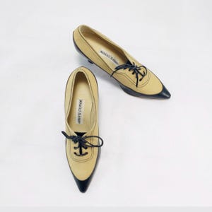 May include: A pair of beige and black pointed-toe shoes with laces. The shoes have a low heel and the brand name "MANOLO BLAHNIK" is printed on the insole.