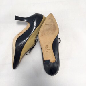 May include: A pair of black and tan leather pumps with pointed toes and a small heel. The shoes are labeled "Manolo Blahnik" and are size 38. The shoes have a classic design.