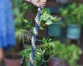 May include: A wooden walking stick with a blue and white snake design. The stick has a brown wooden handle.