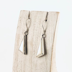 Peut inclure: Une paire de boucles d'oreilles en argent avec des pendentifs triangulaires blancs sur un présentoir en bois.